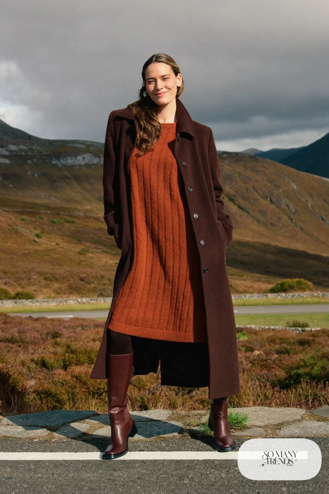 Woman in a rust ribbed knit midi dress, long chocolate brown wool coat, sheer tights and tall brown boots on a Highland roadside, outfit 14