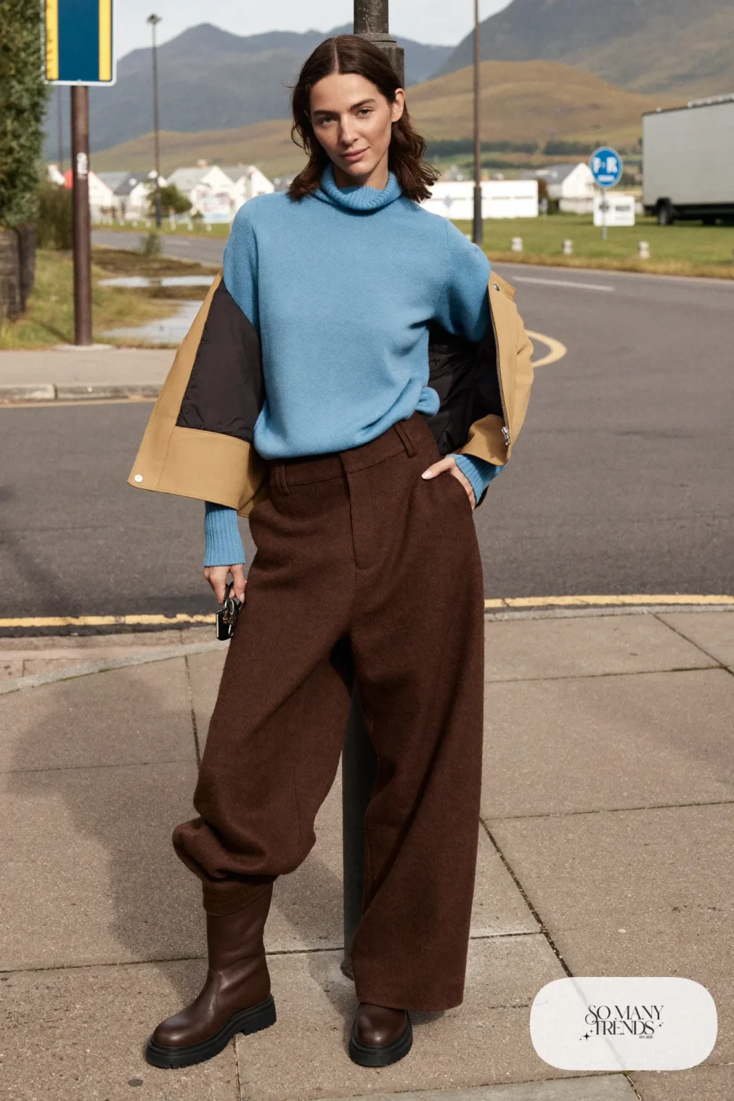 Woman in brown wide-leg wool pants, baby blue roll neck sweater, short sand jacket and brown boots at a Highland village stop, outfit 18