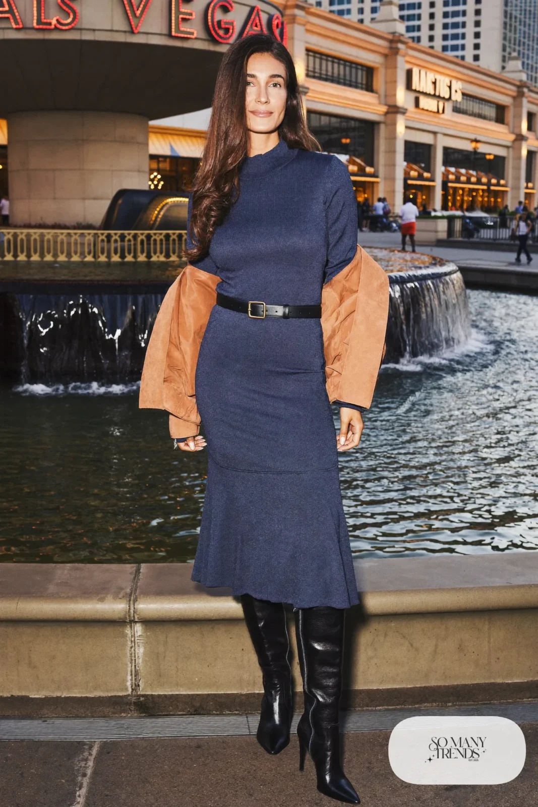 Woman in an indigo knit midi dress with black belt, tall black boots and short jacket in Las Vegas, outfit 12
