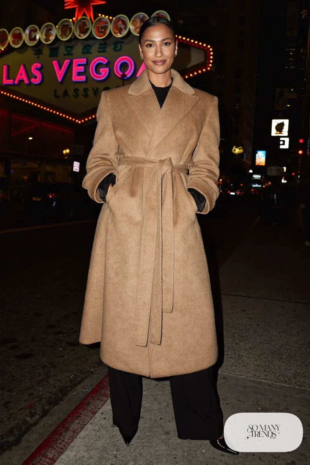 Woman in a belted camel coat over an all-black outfit and pointed pumps in Las Vegas at night, outfit 21