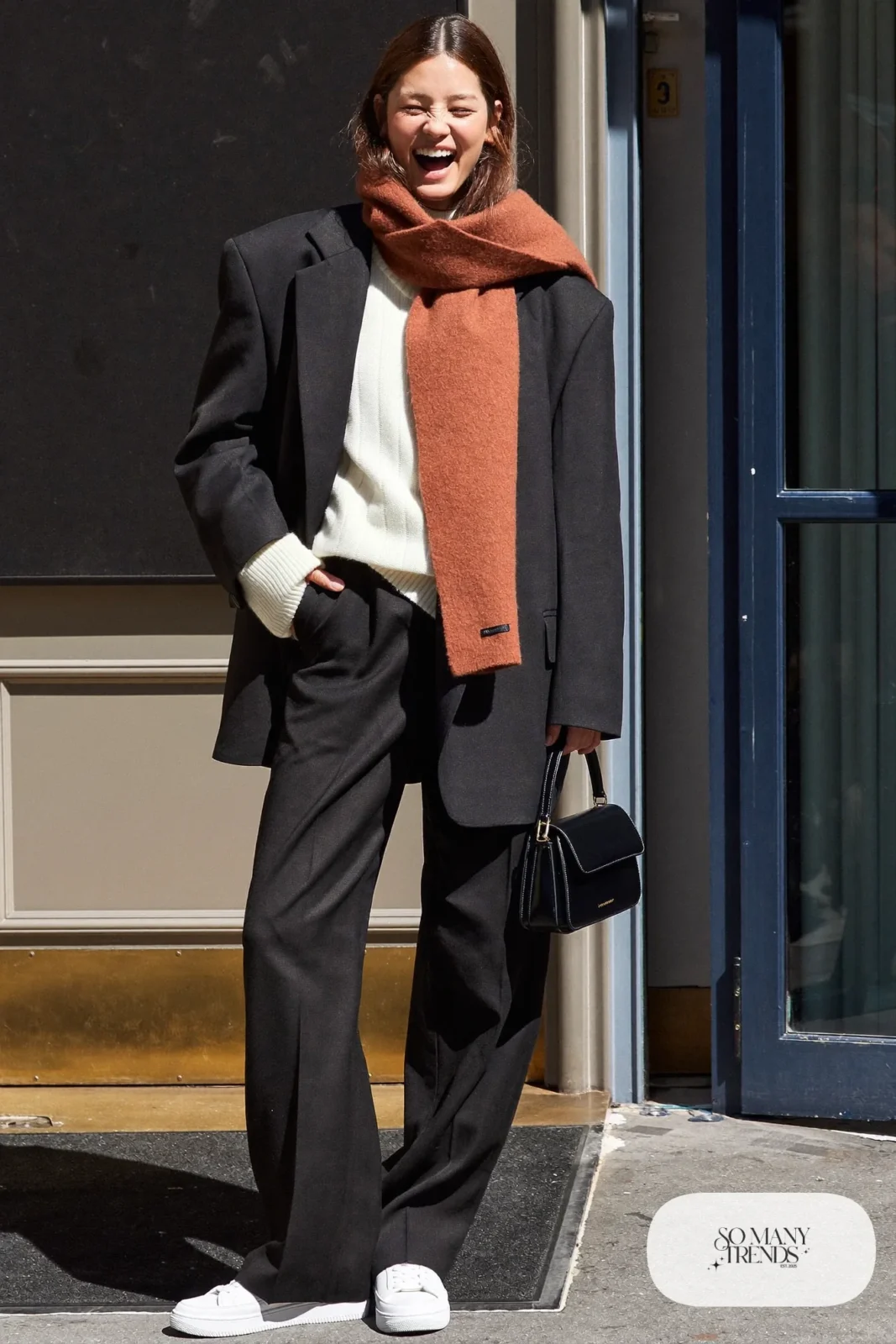 Woman in a black oversized blazer, wide-leg pants, cream knit, terracotta scarf and white sneakers on the Las Vegas Strip, outfit 29