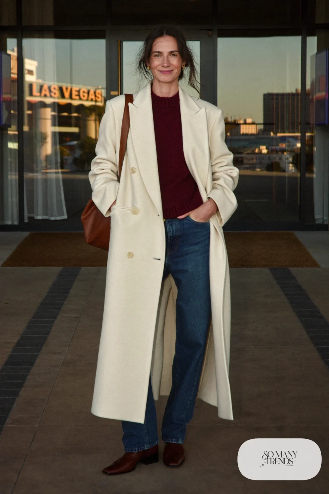 Woman in a long cream wool coat, burgundy knit, indigo jeans and brown ankle boots in Las Vegas, outfit 30