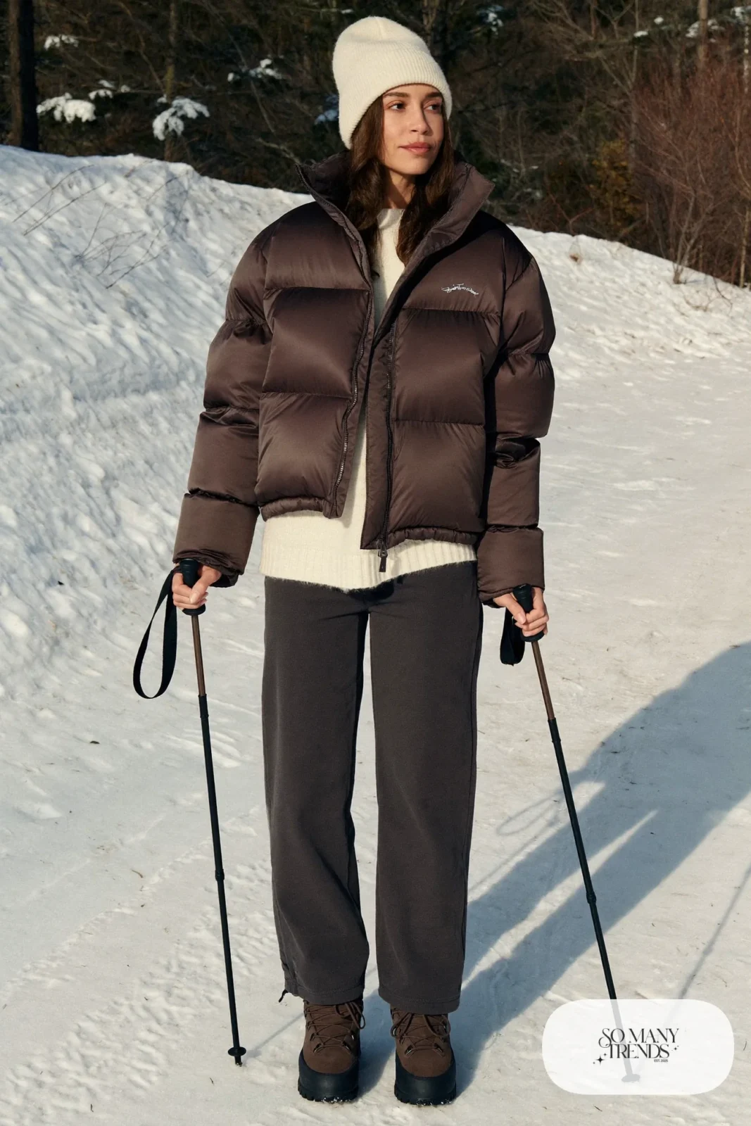 Look 8: cropped chocolate puffer jacket over a cream sweater and charcoal snow pants with brown boots, forest trail