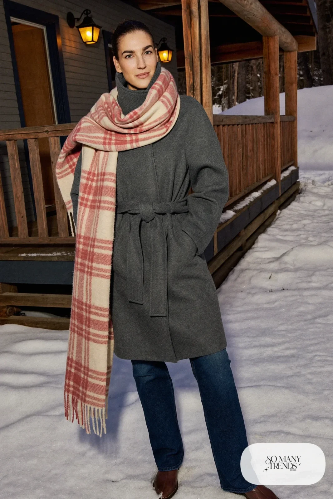 Look 24: gray wool coat with a belt and a rose cream plaid blanket scarf over dark jeans with boots, snowy porch with lanterns