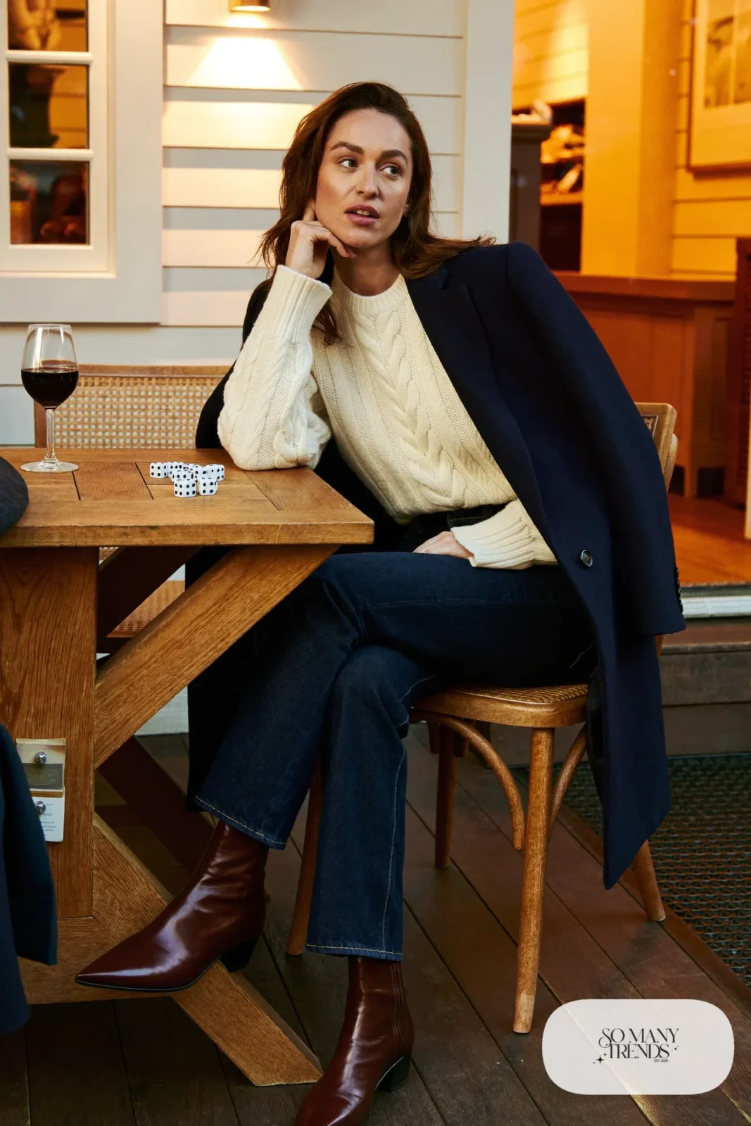 Look 28: navy wool blazer over a cream cable knit sweater and dark jeans with brown boots, cabin game table