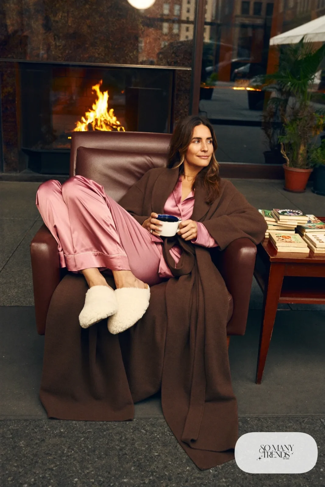 Look 30: rose satin pajama set with a long chocolate wool robe and cream slippers, cabin armchair by the fire