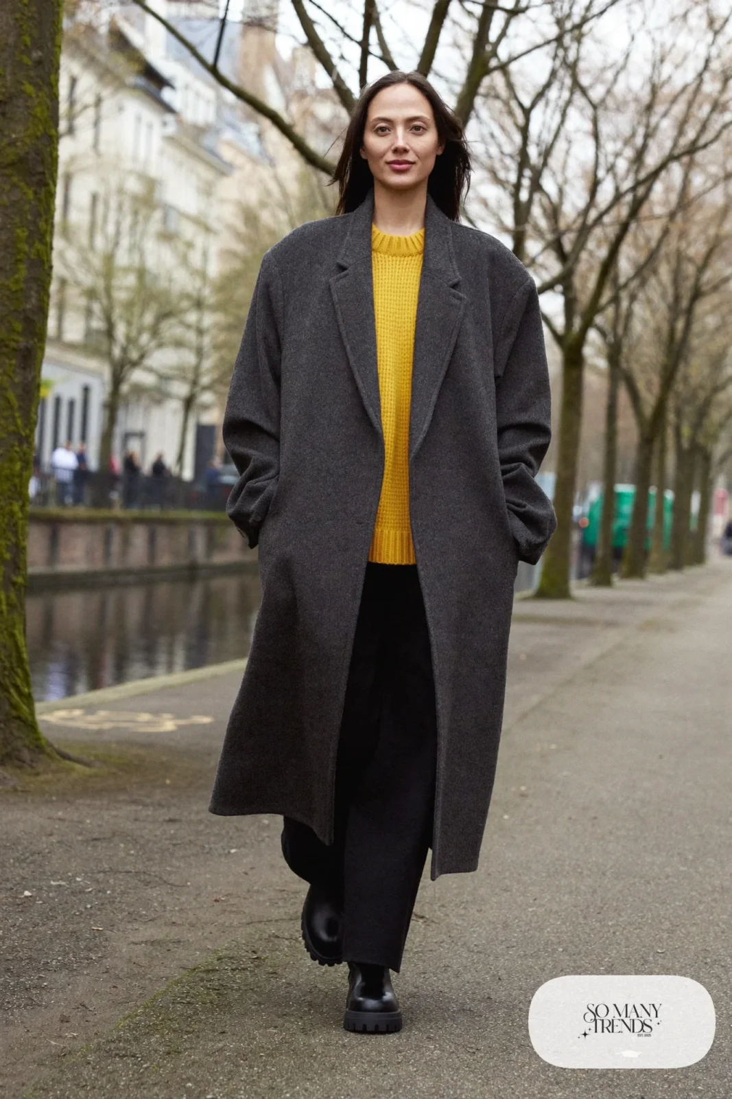 Woman in a charcoal wool coat, mustard knit sweater, wide black pants and black chunky boots on a canal path, outfit 5