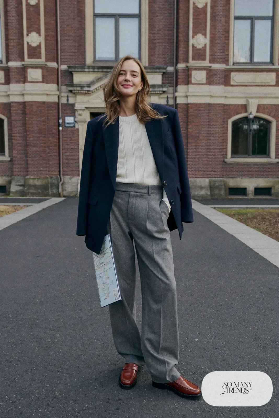 Woman in a navy wool blazer, cream ribbed sweater, wide gray pants and brown lug-sole loafers in a museum courtyard, outfit 7