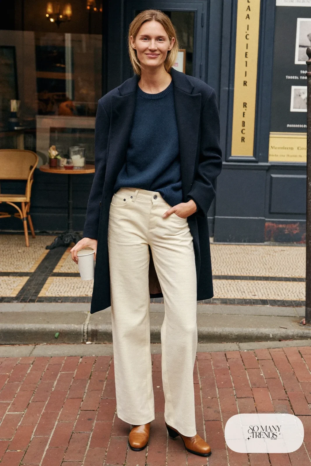 Woman in ivory wide-leg pants, navy sweater, dark wool coat and brown leather boots outside a museum cafe, outfit 12