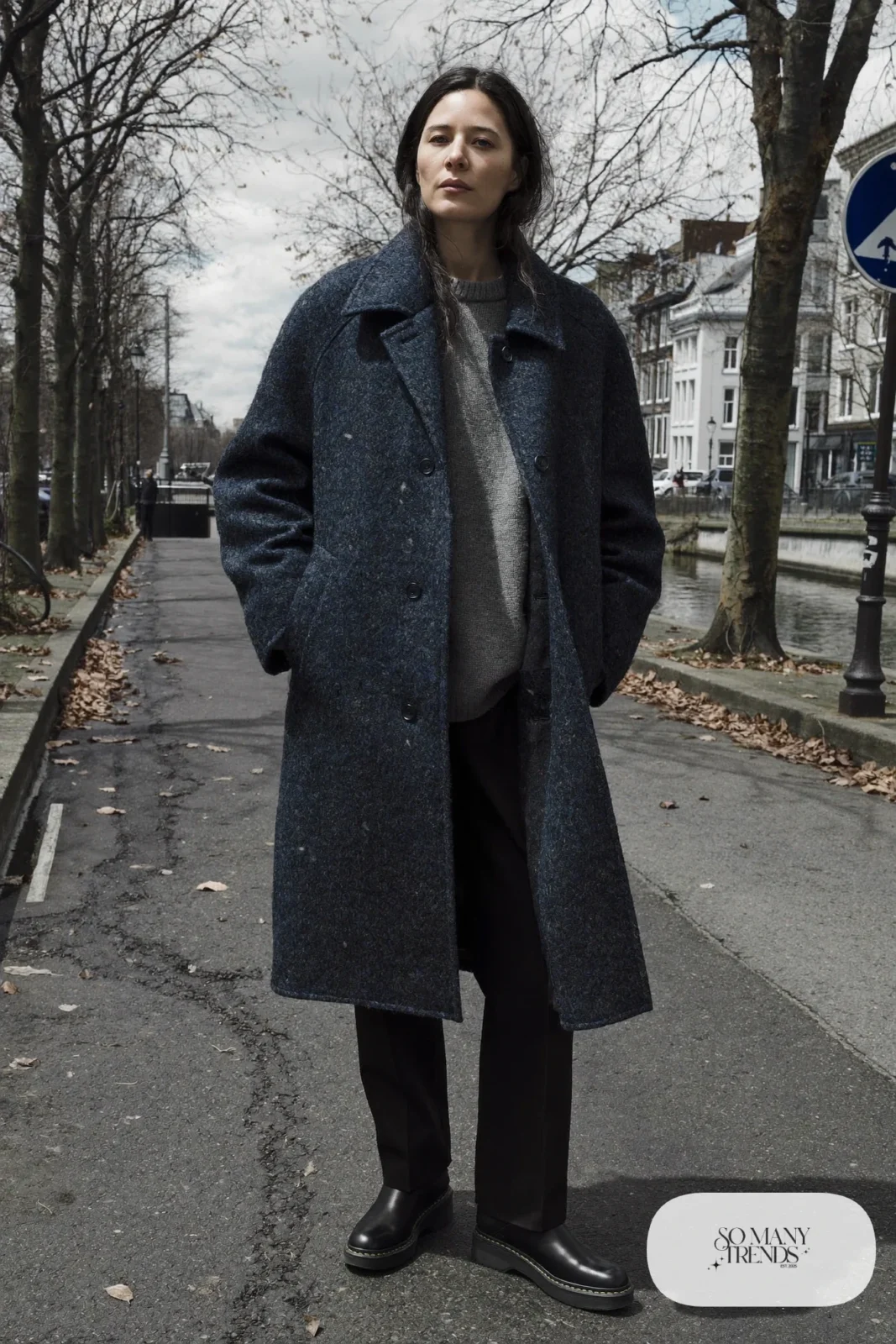 Woman in a navy wool coat, gray knit, straight black pants, black grip-sole boots and beanie standing by a bicycle, outfit 17