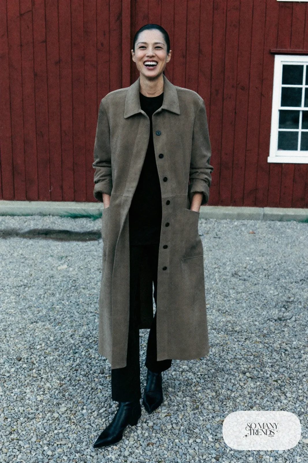 Woman in a taupe long suede duster, black knit top and pants and black boots, outfit 5