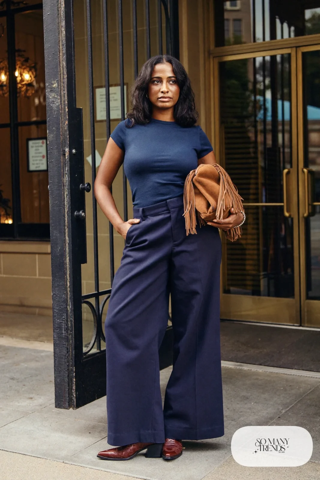 Woman in navy fitted knit top, navy wide-leg pants, camel fringe crossbody bag and brown stitched cowboy boots, outfit 4