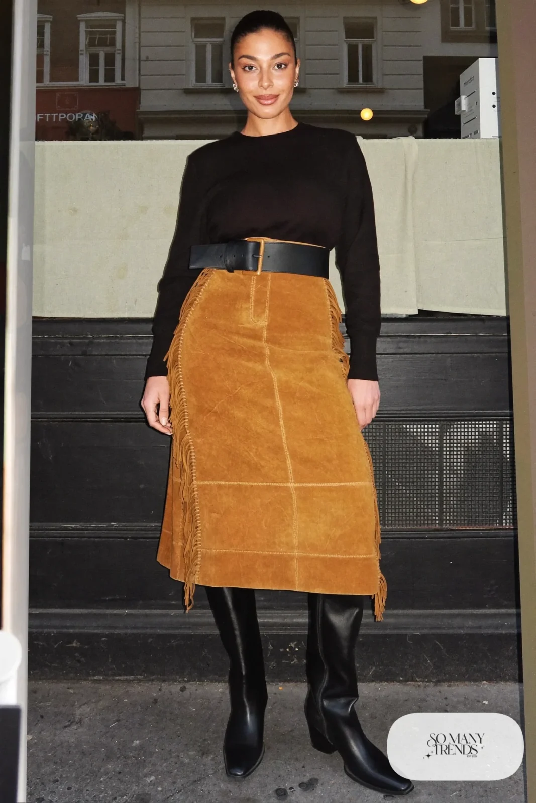 Woman in camel suede fringe midi skirt, fitted black long-sleeve top, wide belt and tall black boots, outfit 15