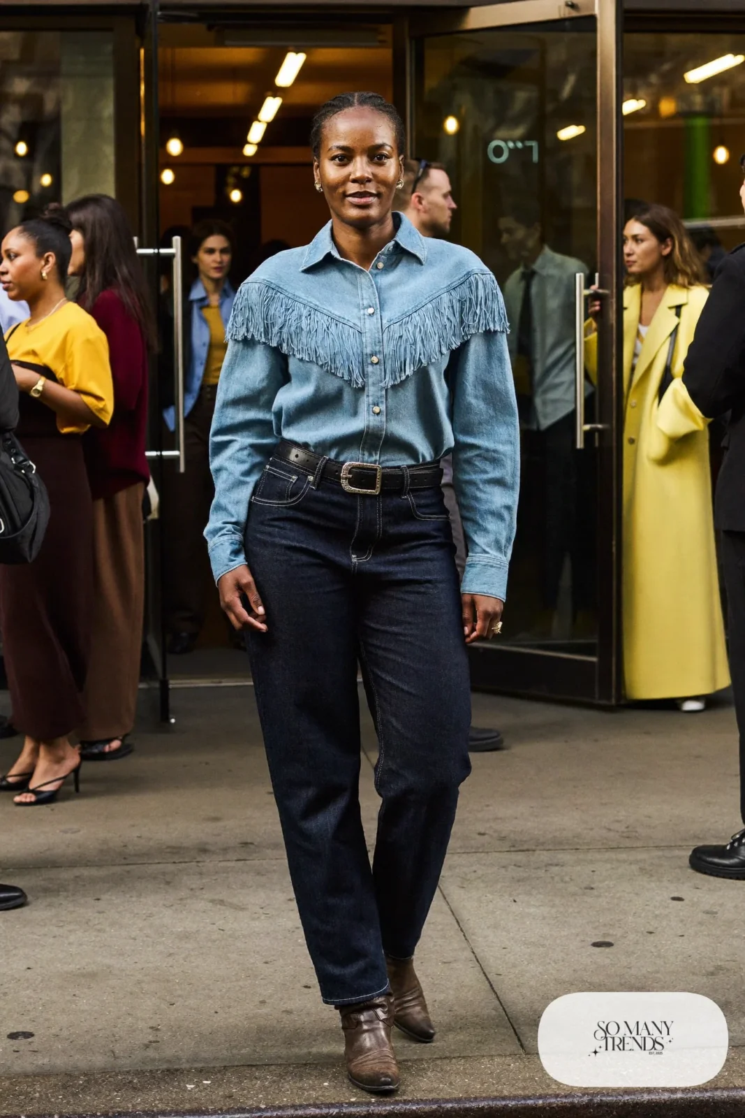 Woman in light denim fringe yoke shirt, dark jeans, silver buckle belt and brown cowboy boots, outfit 21