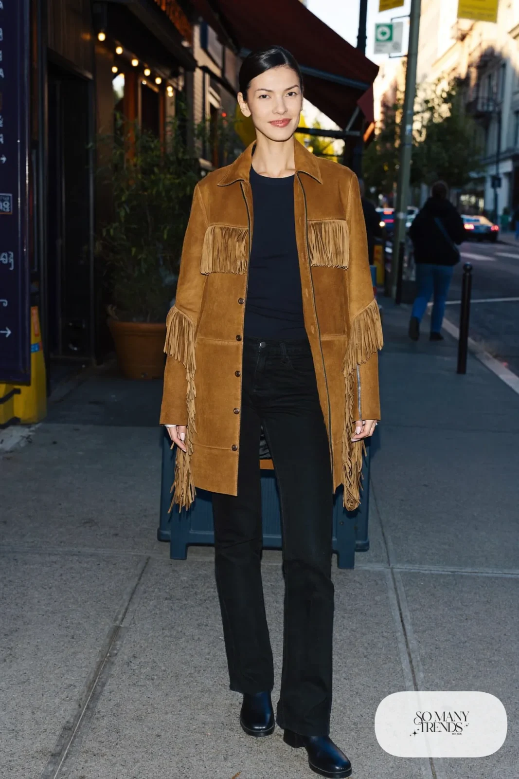 Woman in camel suede fringe jacket, black tee, black straight pants and black stacked heel boots, outfit 22