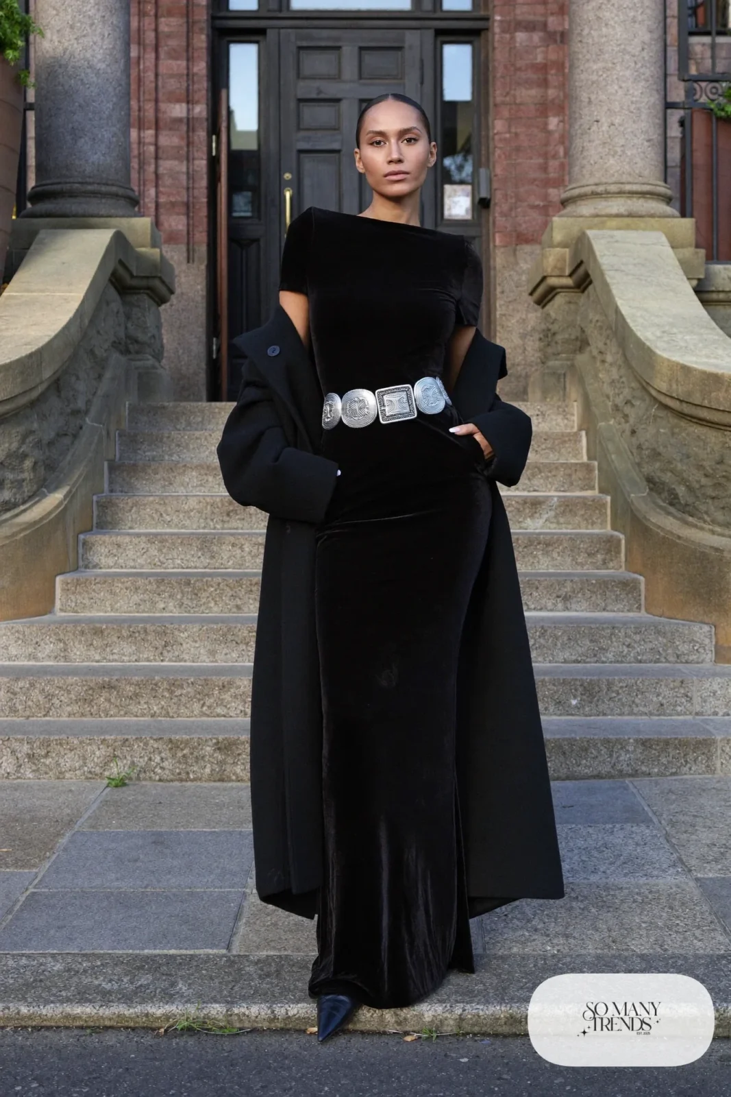 Woman in a black velvet column gown with a silver concho belt and black pointed boots, western gala outfit 1