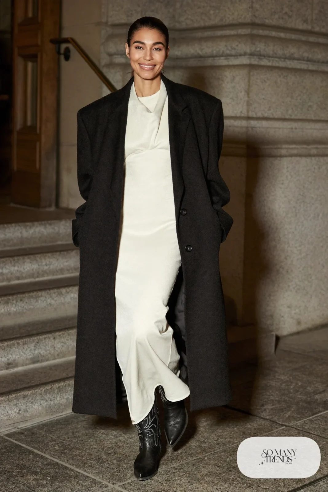 Woman in an ivory long-sleeve gown with embroidered black boots and a black wool coat, western gala outfit 18