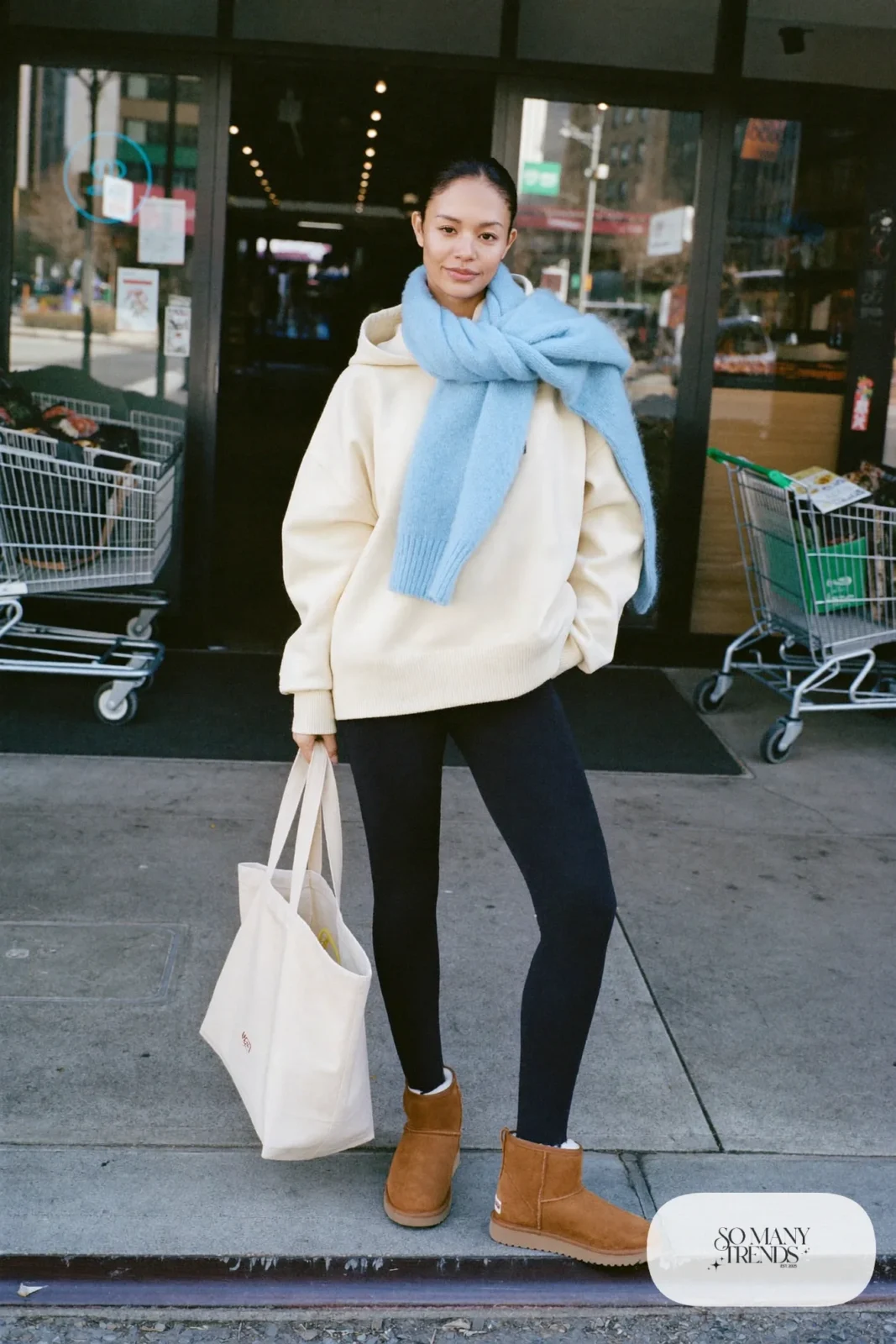 Woman in black leggings, oversized cream hoodie, sky blue scarf and chestnut Ugg mini boots, outfit 11