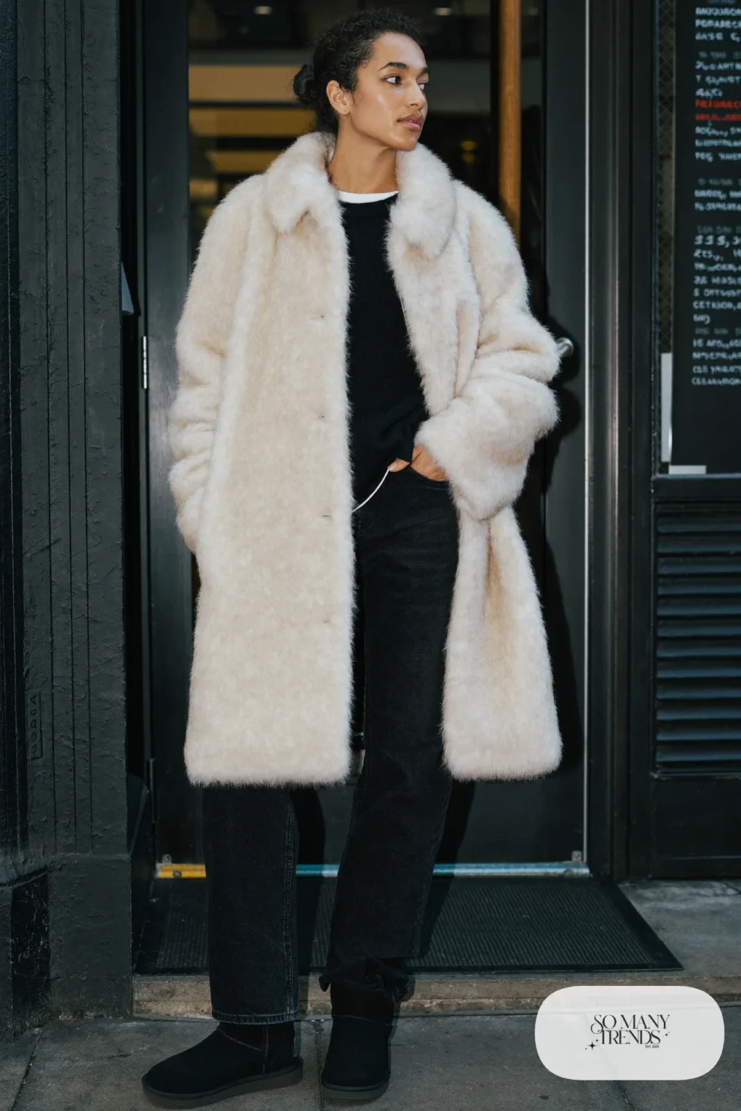 Woman in black straight jeans, black knit sweater, cream faux fur coat and black Ugg mini boots, outfit 15