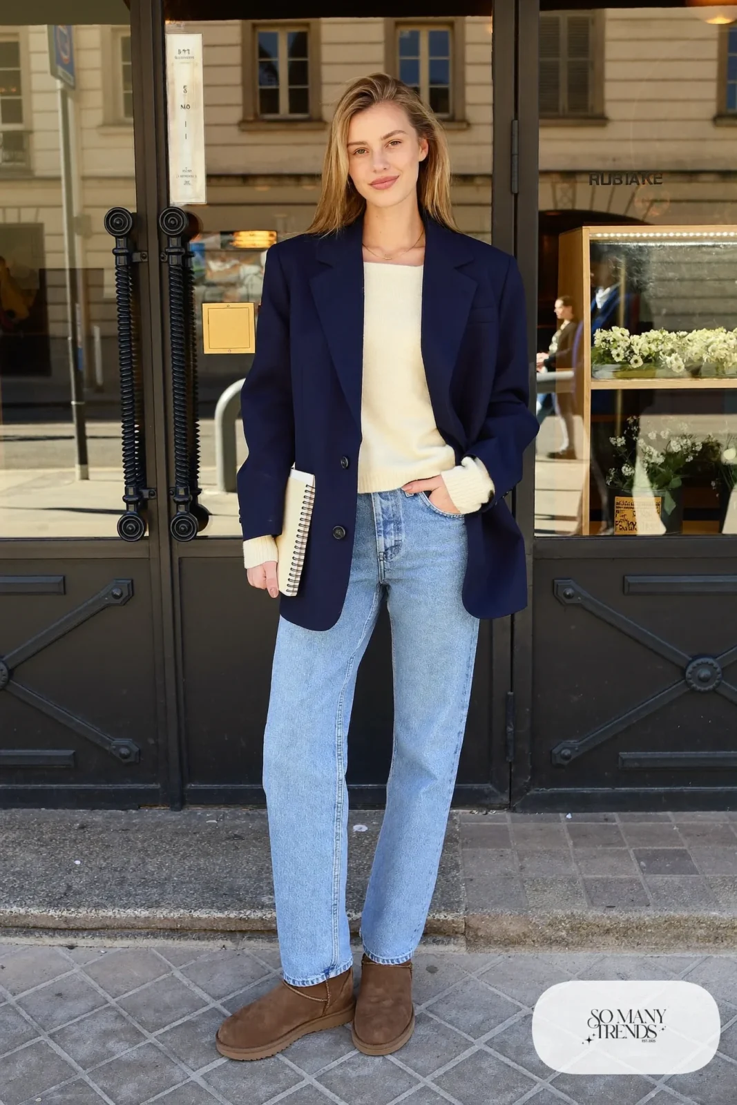 Woman in light blue straight jeans, cream knit, navy blazer and chocolate Ugg mini boots, outfit 17