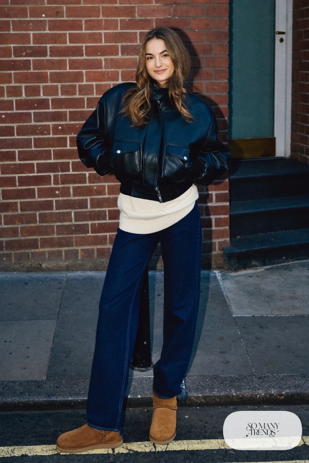 Woman in dark straight jeans, cream knit, black leather jacket and chestnut Ugg mini boots, outfit 22