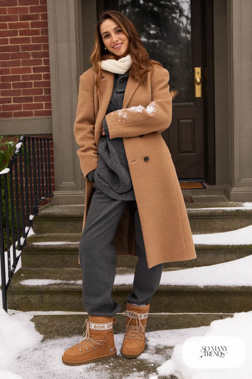 Woman in a long camel wool coat, charcoal cable knit sweater, gray straight pants and tan Sorel snow boots, outfit 1
