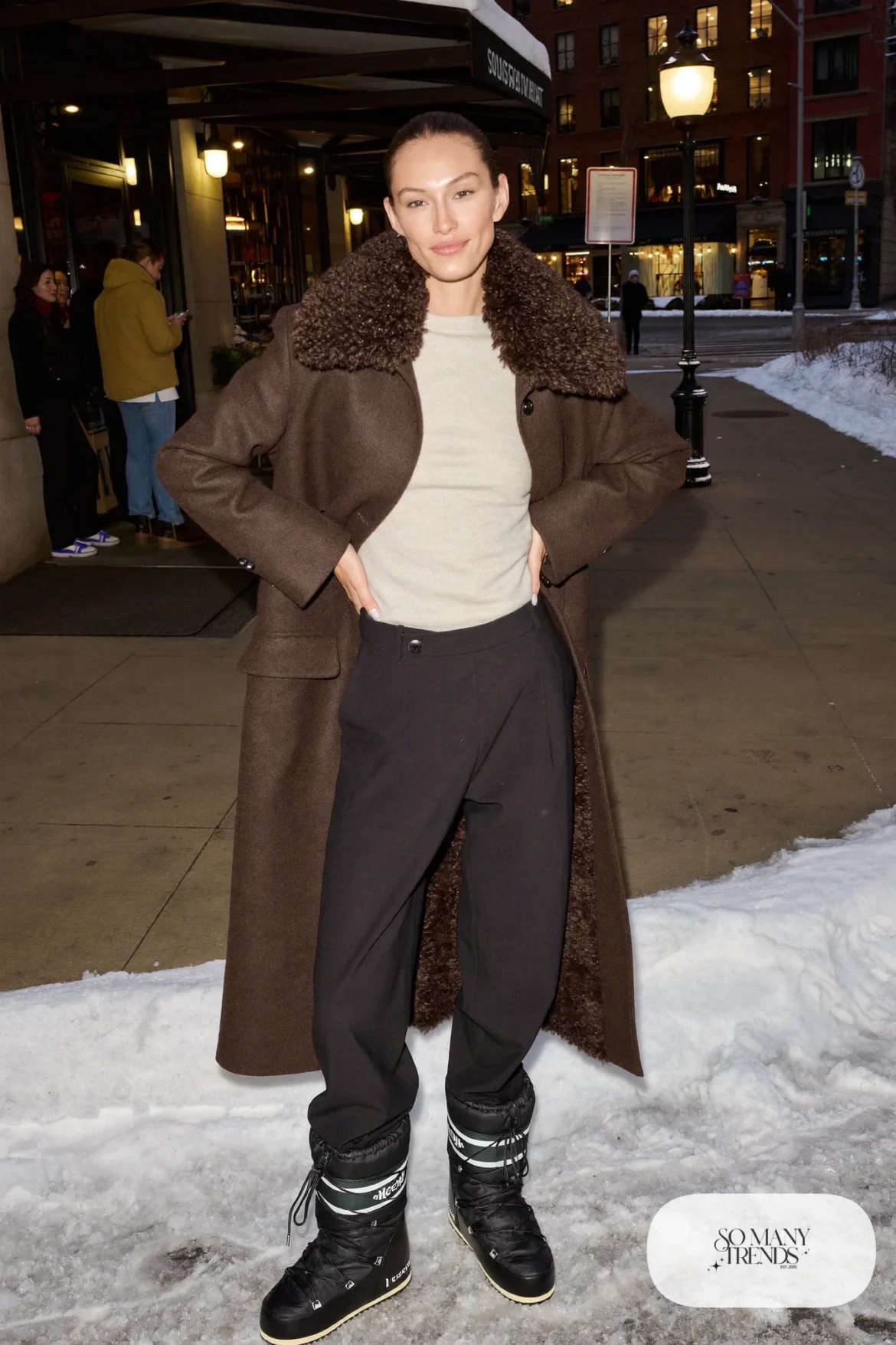 Woman in a chocolate brown coat with shearling collar, black wool pants, cream knit and black Sorel boots, outfit 8