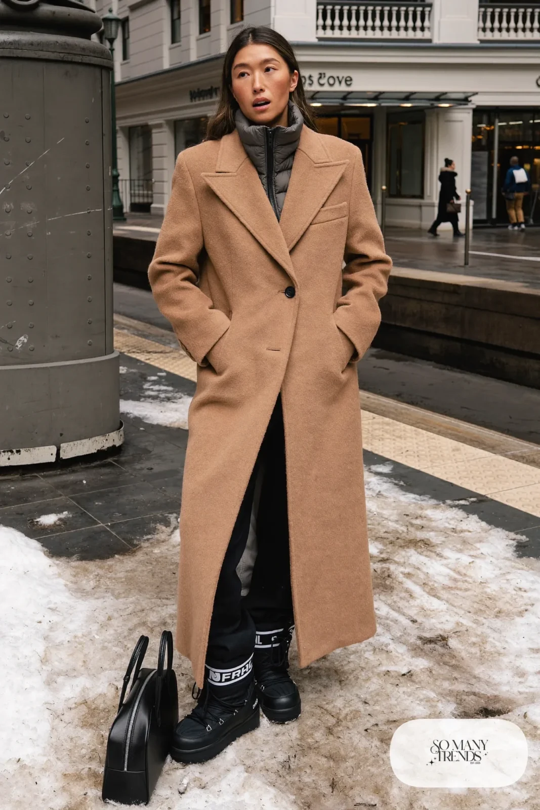 Woman in a camel overcoat over a charcoal quilted liner jacket, black pants and black Sorel boots, outfit 16