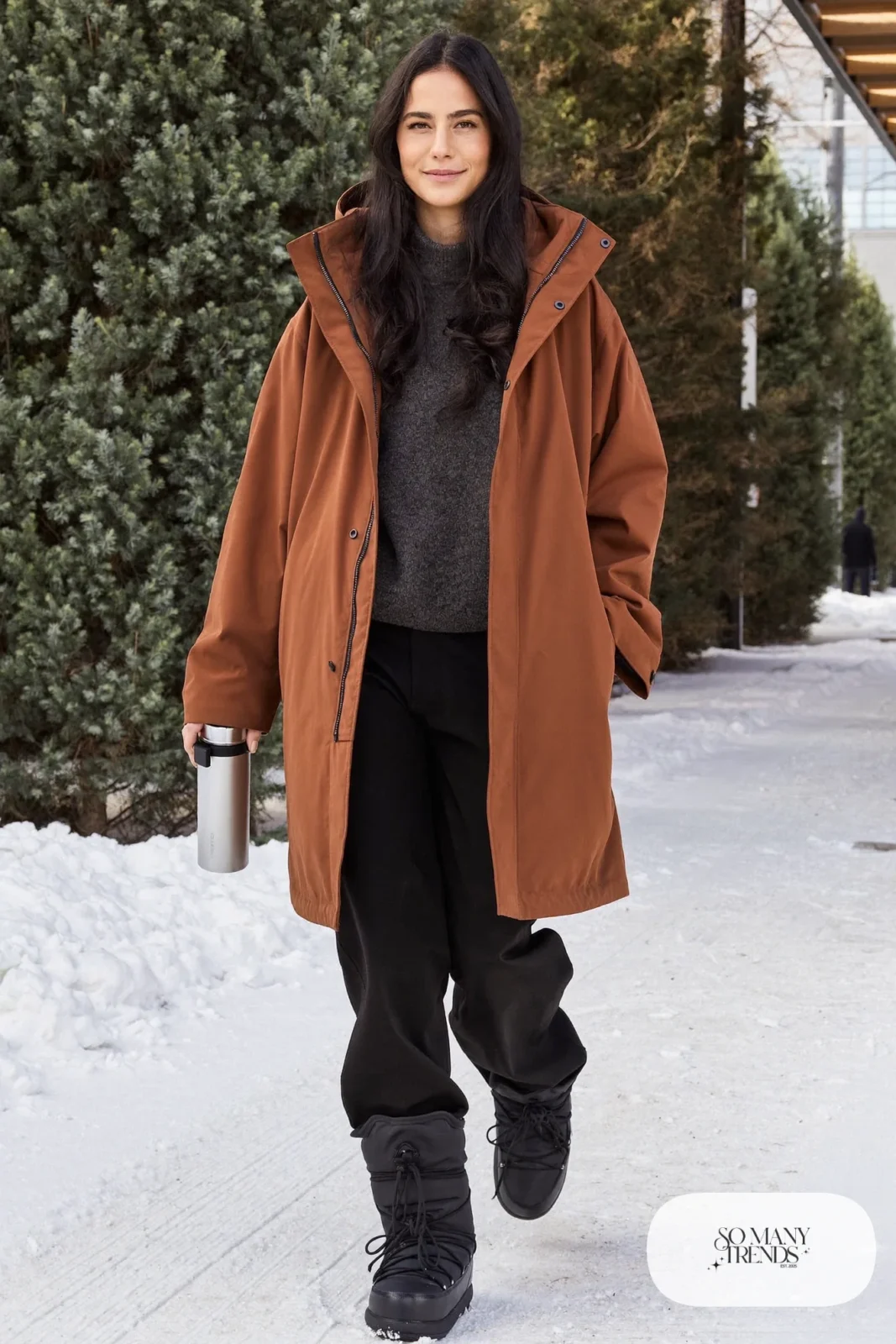 Woman in a rust parka, black wide-leg pants, charcoal sweater and black Sorel boots, outfit 21
