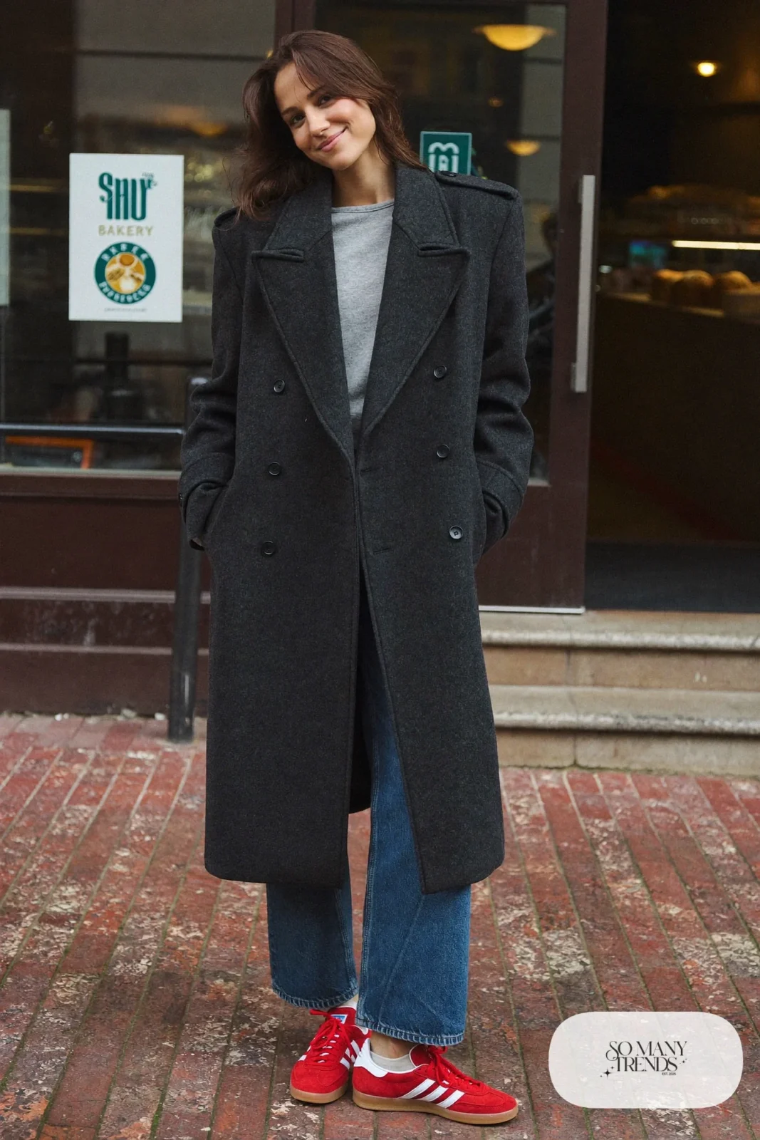 Woman in a charcoal wool peacoat, gray crewneck sweater, washed barrel jeans and red Adidas Gazelle sneakers, outfit 1