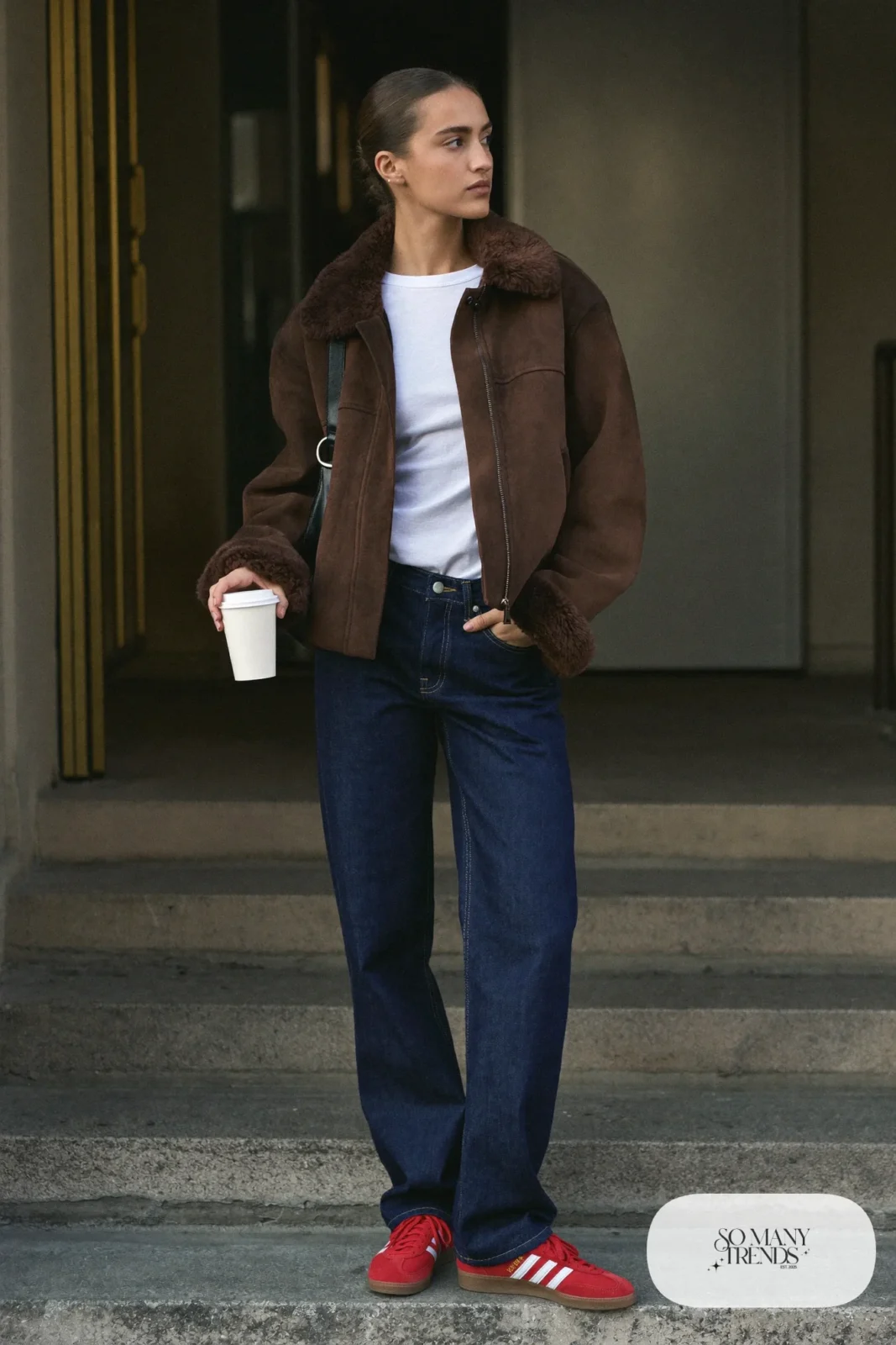 Woman in a cropped brown shearling jacket, white long-sleeve tee, straight dark jeans and red Adidas Gazelle sneakers, outfit 2