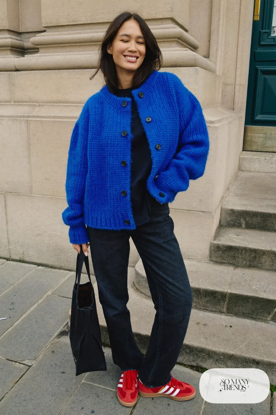 Woman in a cobalt blue chunky cardigan, black tee, black straight jeans and red Adidas Gazelle sneakers, outfit 5