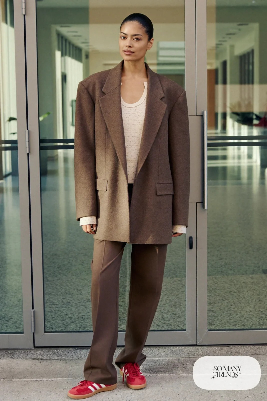 Woman in a chocolate brown blazer, matching brown straight pants, cream knit tank and red Adidas Gazelle sneakers, outfit 9