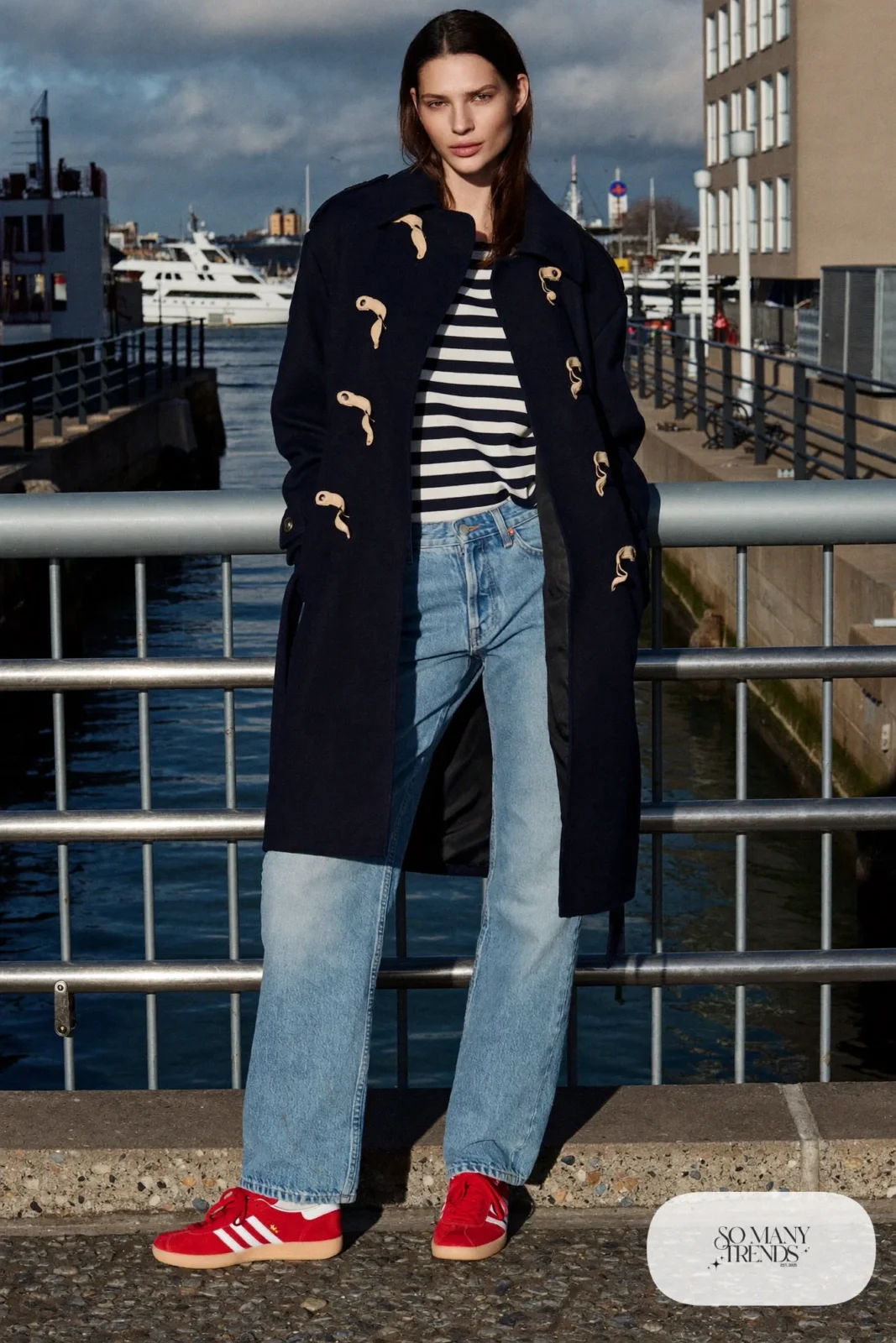 Woman in a navy duffle coat, striped long-sleeve tee, light-wash straight jeans and red Adidas Gazelle sneakers, outfit 21