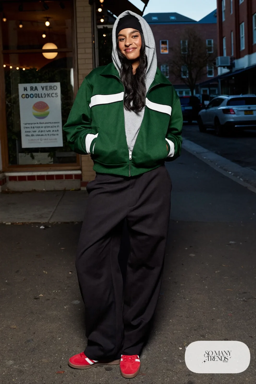 Woman in a green track jacket, gray hoodie, wide black pants and red Adidas Gazelle sneakers, outfit 26