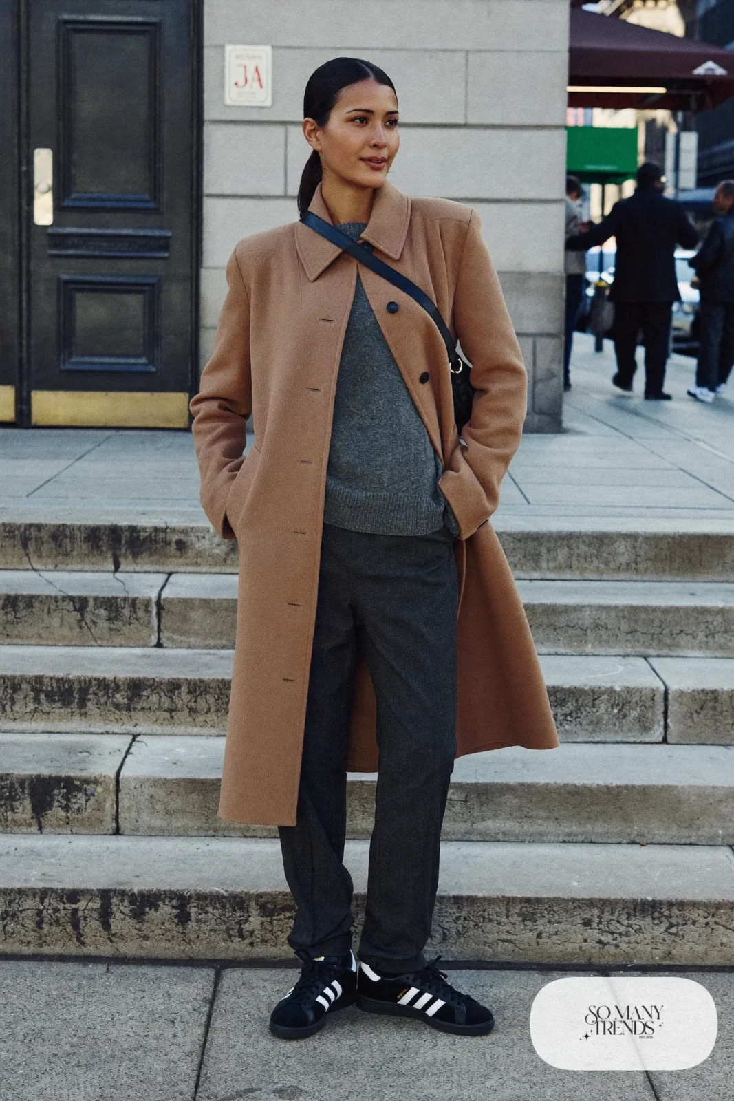 Woman in long camel wool coat, gray knit sweater, straight charcoal pants and black Adidas Campus sneakers, outfit 1