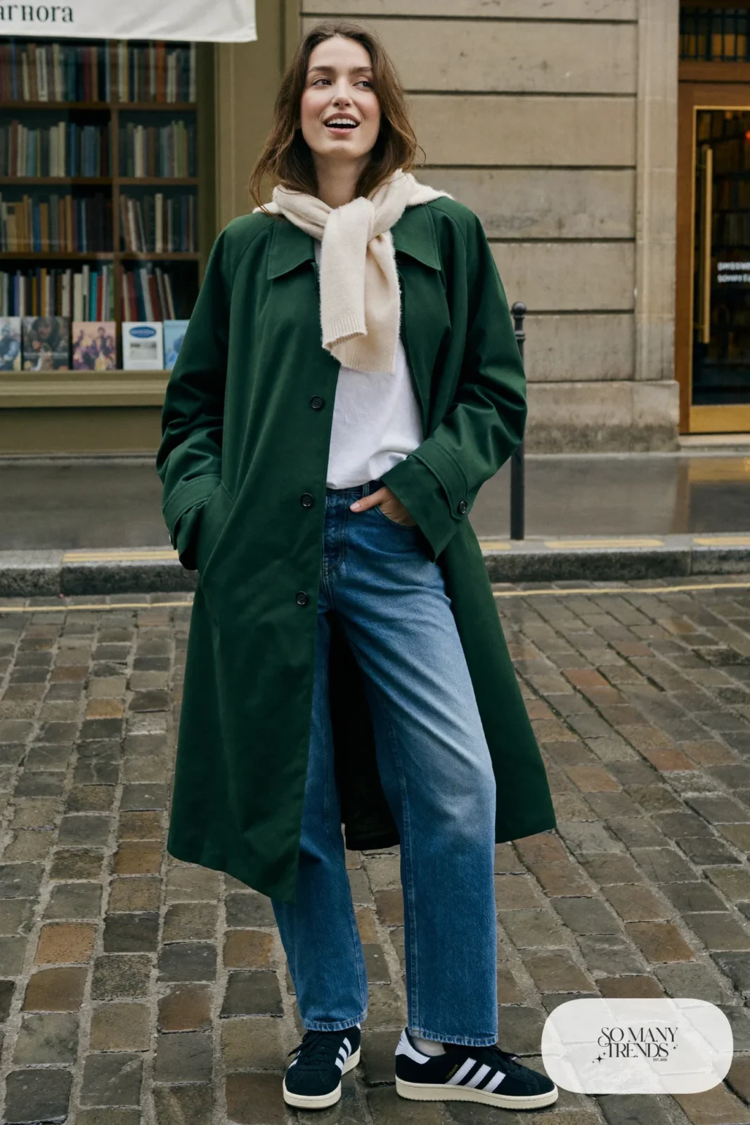 Woman in forest green trench coat, white tee, straight blue jeans, cream scarf and black Adidas Campus sneakers, outfit 3