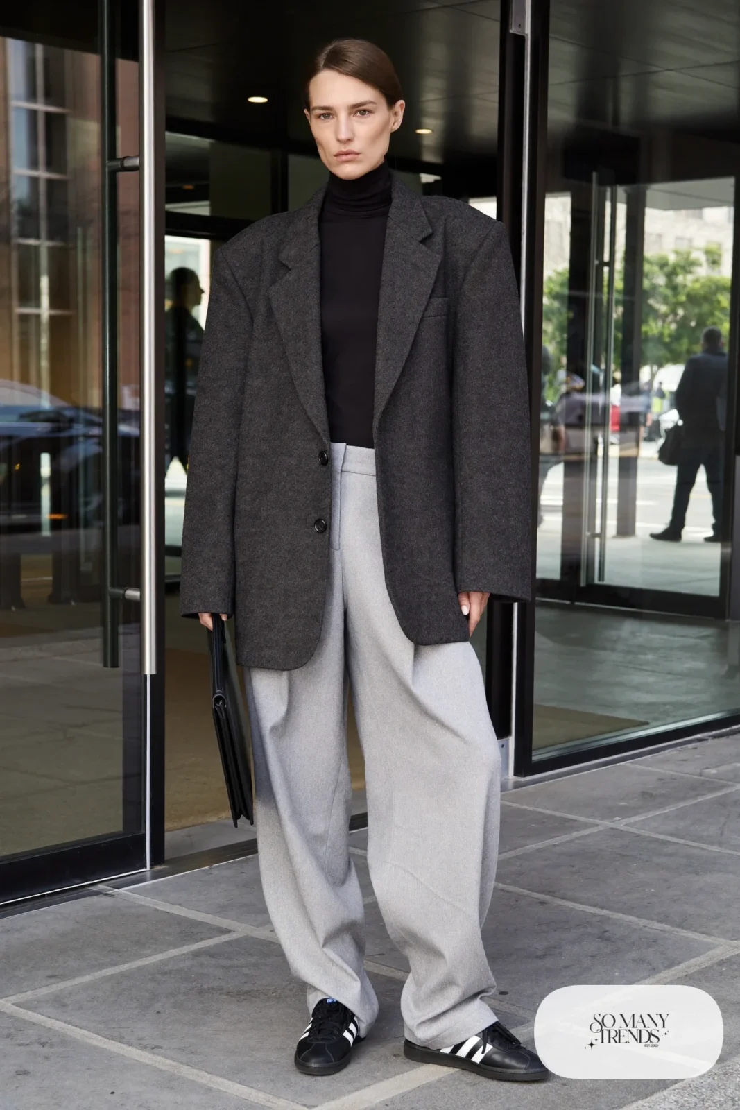 Woman in oversized charcoal blazer, black turtleneck, wide pleated gray pants and black Adidas Campus sneakers, outfit 4