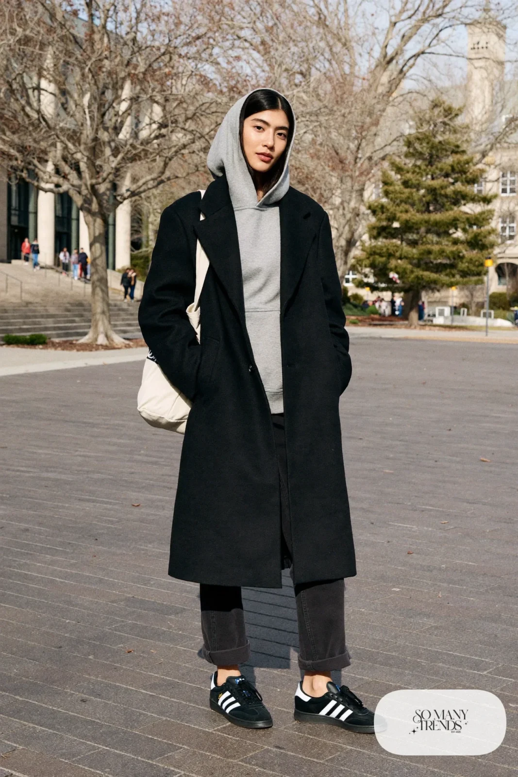 Woman in black overcoat, gray hoodie, dark straight pants and black Adidas Campus sneakers, outfit 6