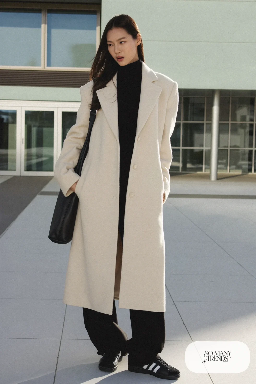 Woman in long ivory wool coat over black turtleneck, black wide pants and black Adidas Campus sneakers, outfit 9