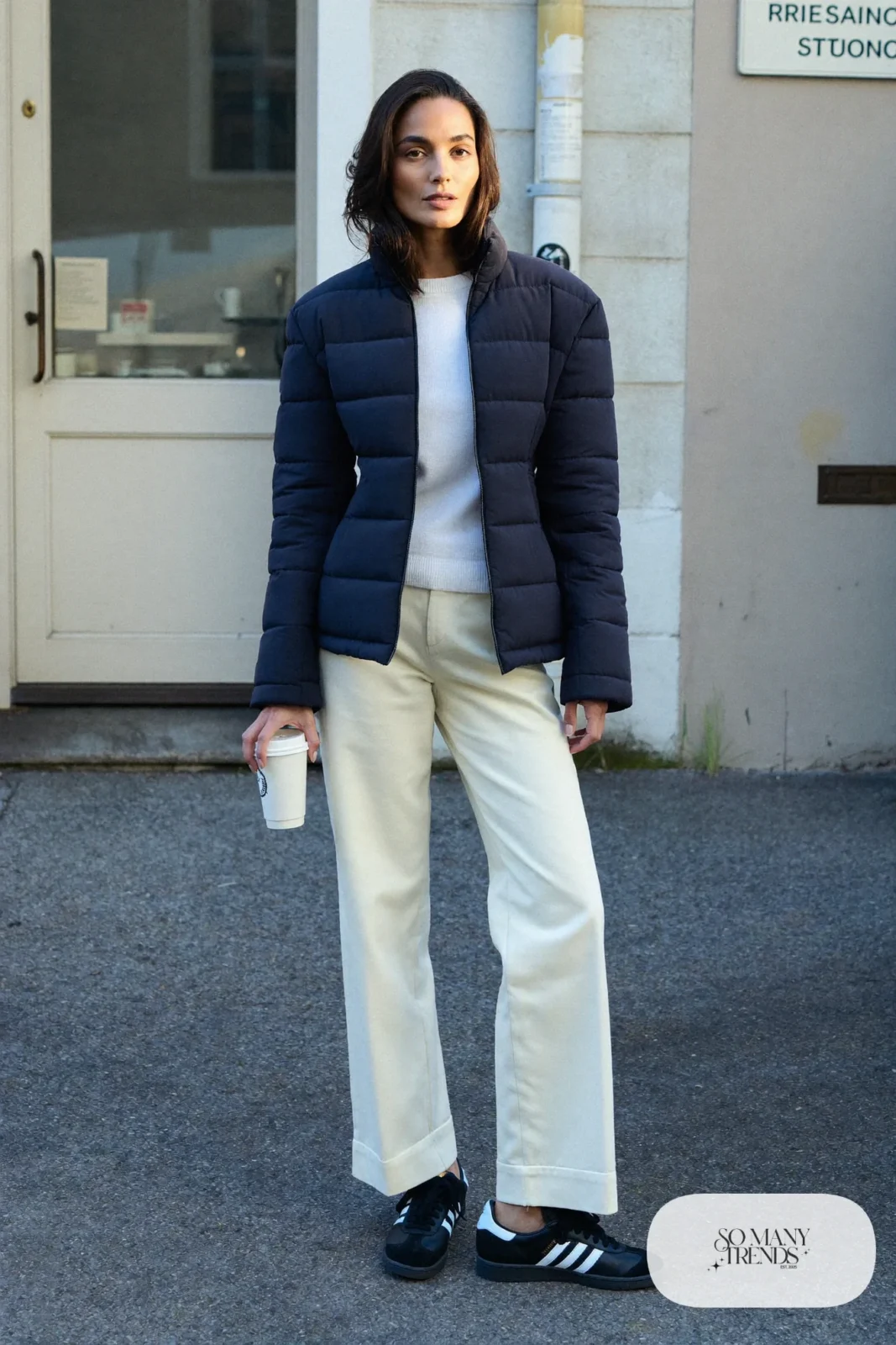 Woman in navy quilted jacket, cream twill pants, white knit and black Adidas Campus sneakers, outfit 15