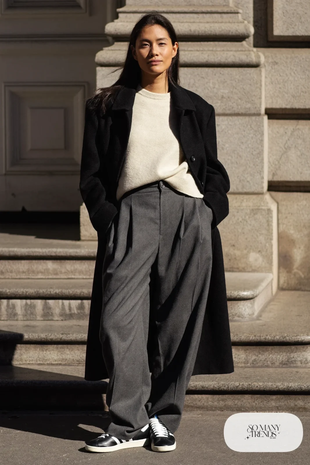 Woman in black coat, tucked cream knit, wide gray flannel pants and black Adidas Campus sneakers, outfit 19