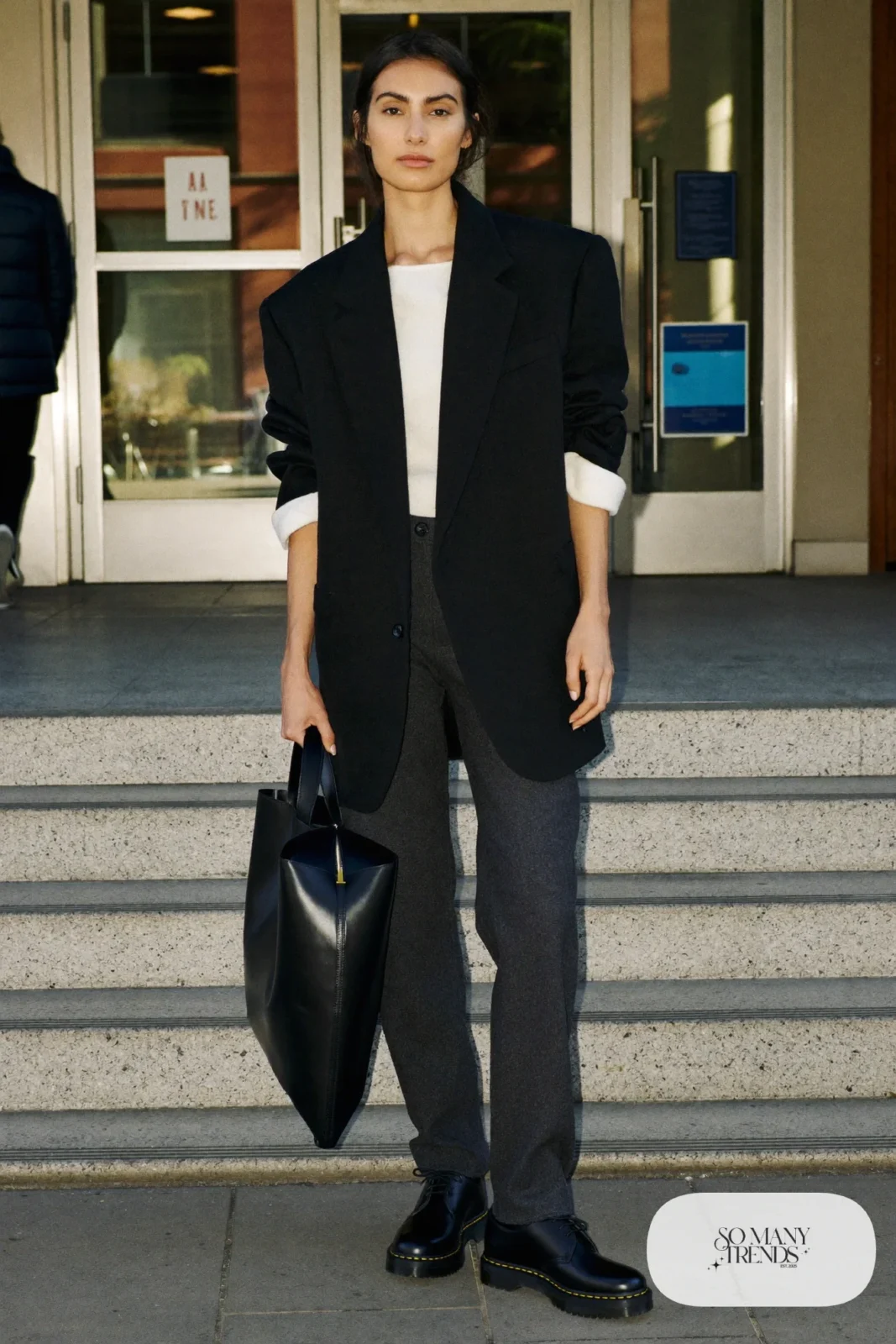 Woman in black oversized wool blazer, ivory knit, charcoal straight pants and cognac Doc Martens loafers, outfit 1