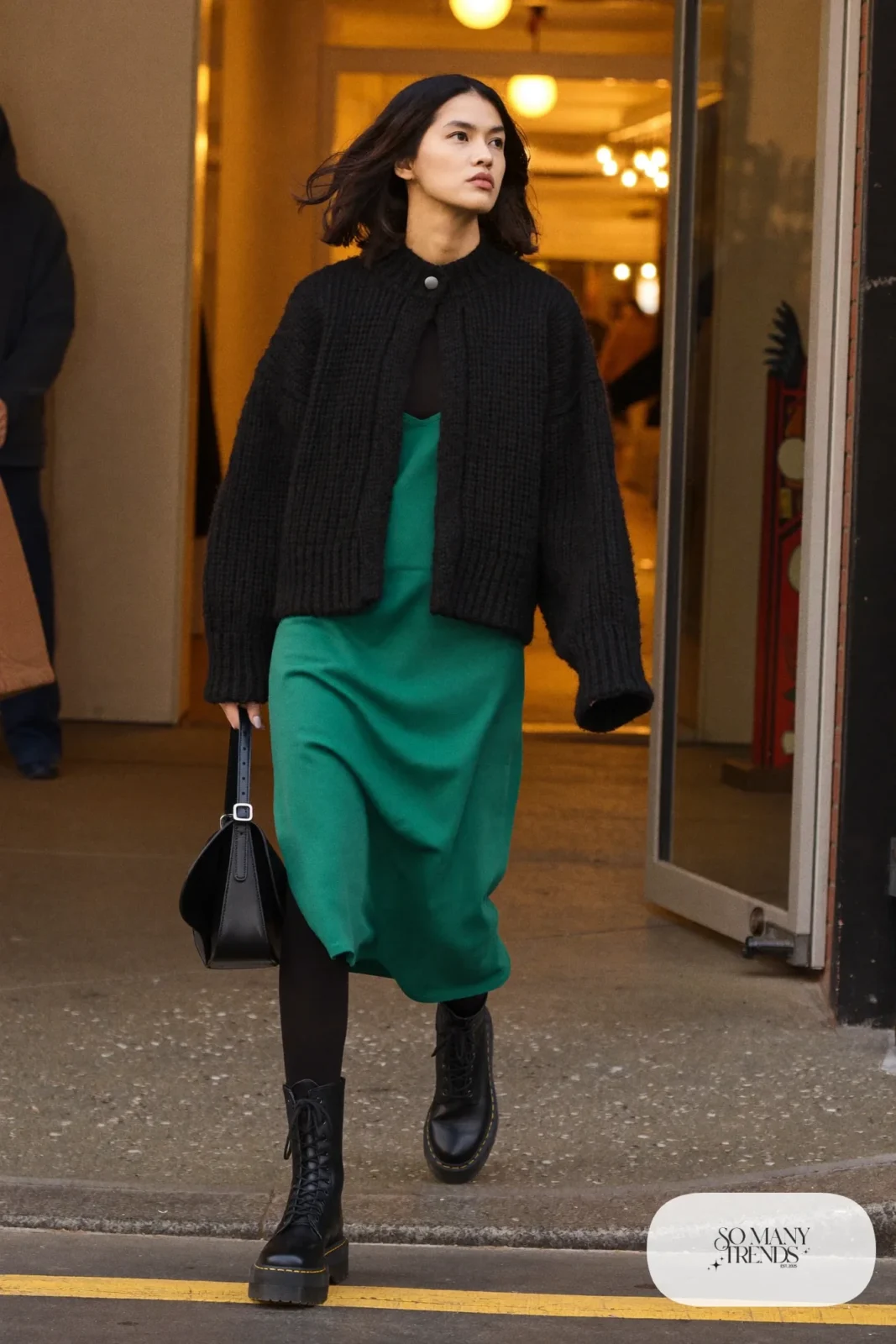 Woman in emerald knit slip dress, oversized black cardigan, opaque black tights and black Doc Martens boots, outfit 13