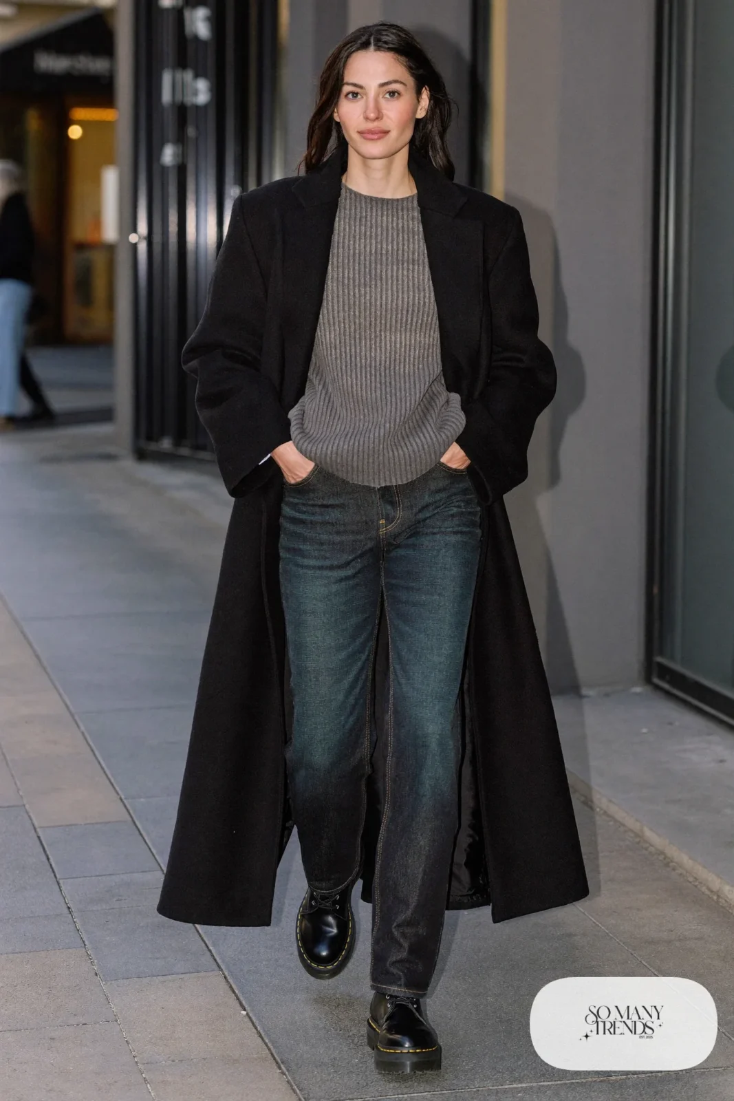 Woman in long black wool coat, gray knit sweater, dark straight jeans and black Doc Martens boots, outfit 14