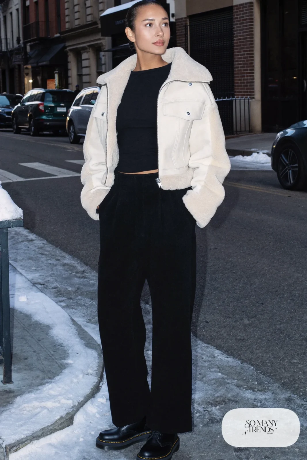 Woman in cropped shearling jacket, fine black knit, high-waisted black pants and black Doc Martens boots, outfit 15