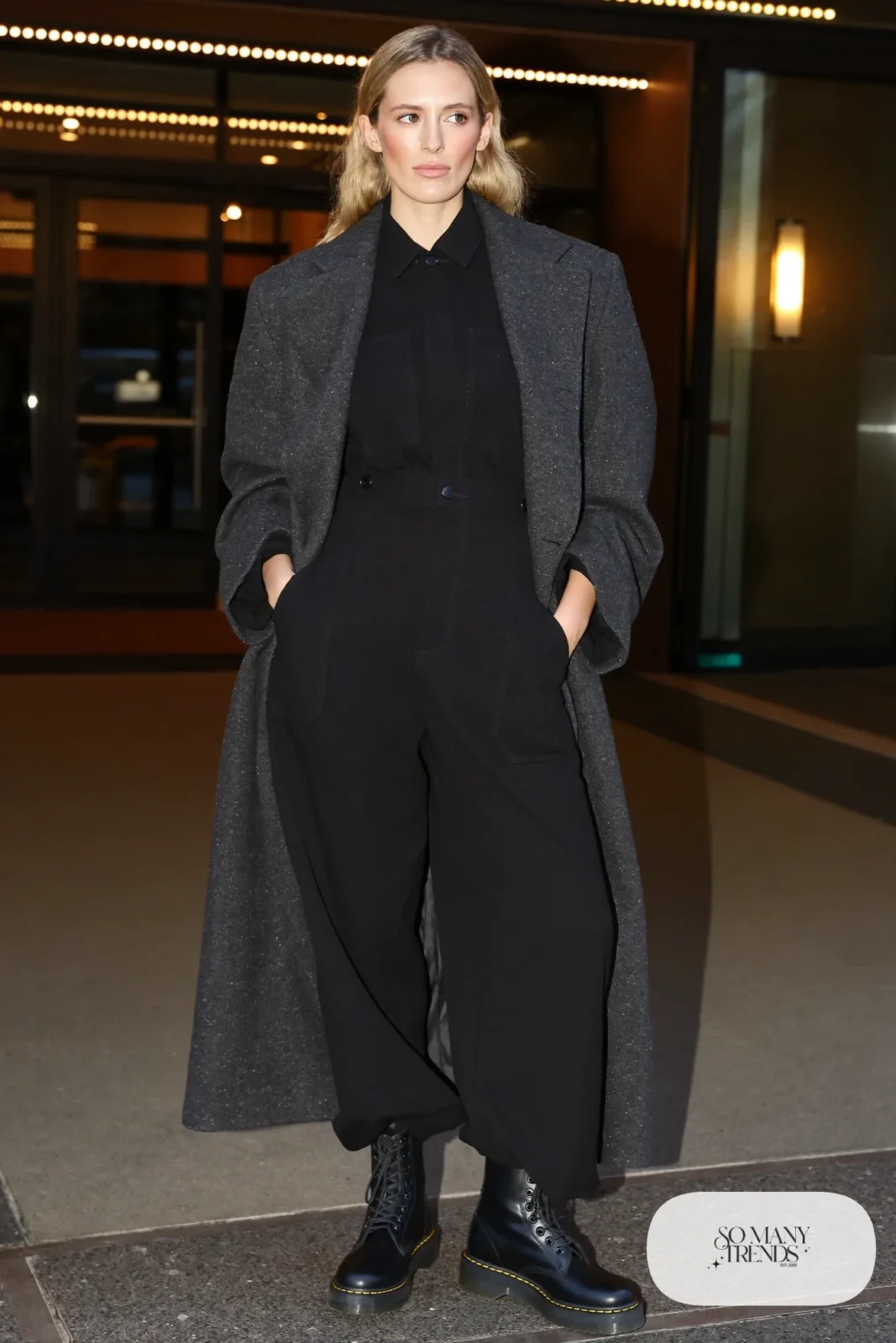 Woman in black wide-leg jumpsuit with belt, long charcoal coat and black Doc Martens boots, outfit 25