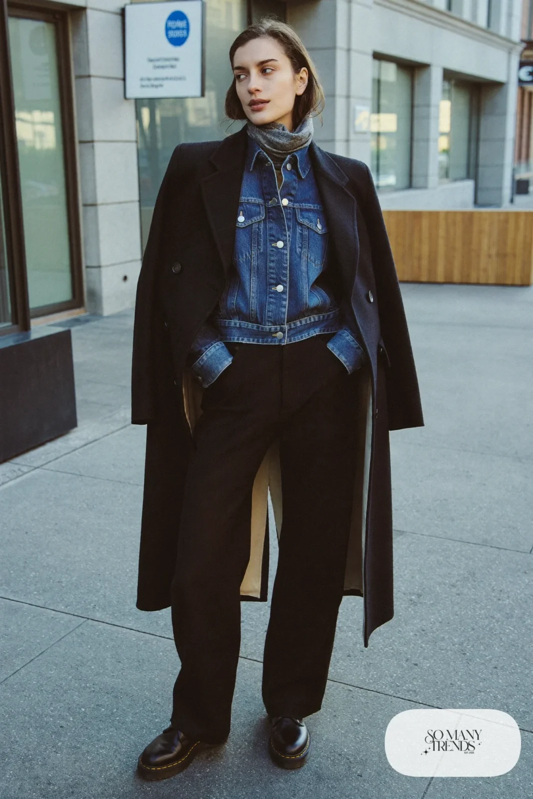 Woman in mid-blue denim jacket, long black wool coat, black pants and black Doc Martens loafers, outfit 28