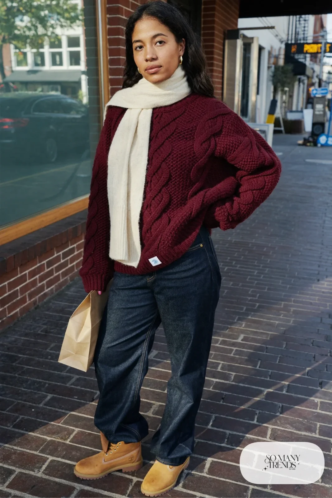 Woman in burgundy cable-knit sweater, dark straight-leg jeans and wheat Timberland-style boots, outfit 1