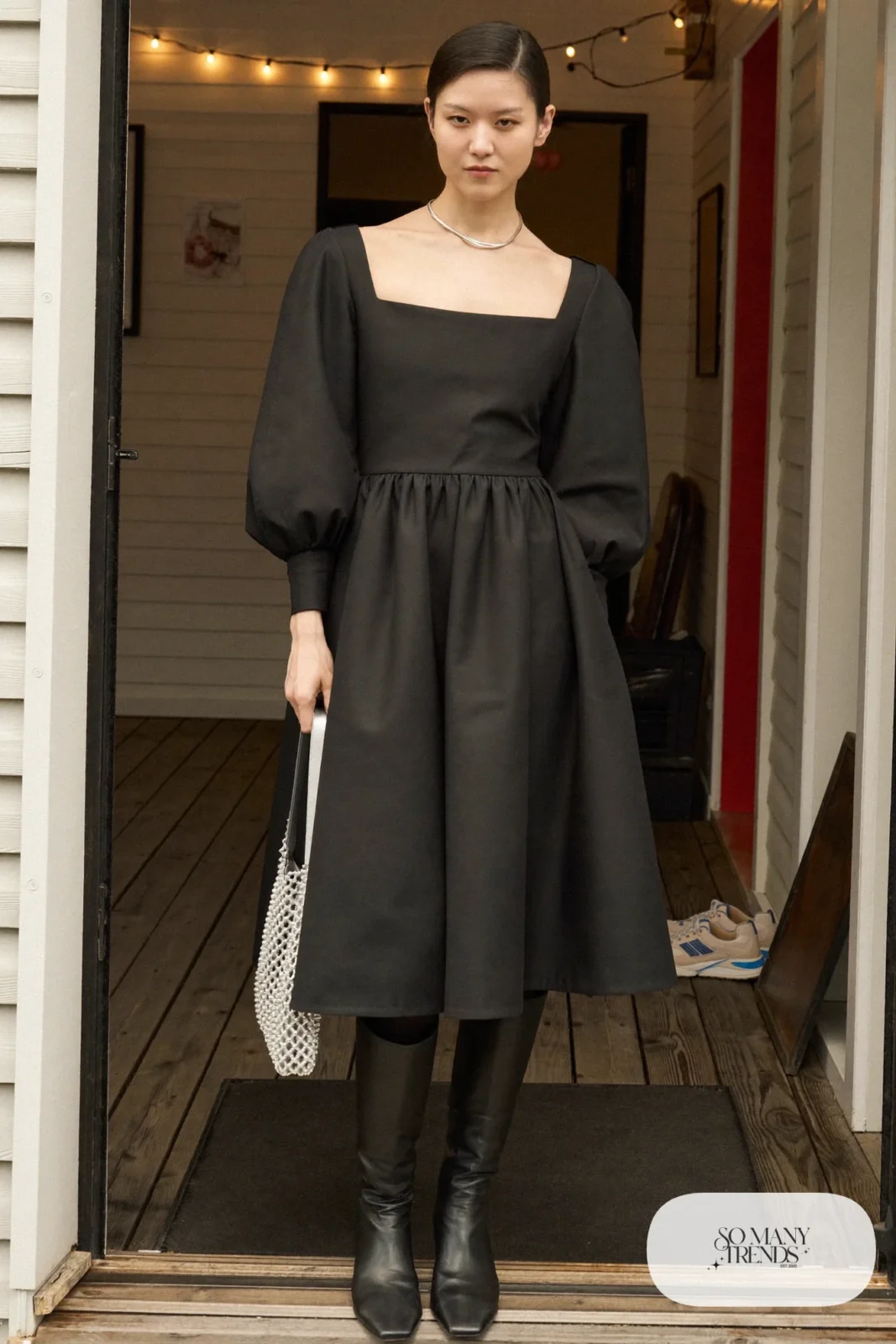 Woman in a black long sleeve midi dress holding a silver mesh bag with black tall boots, New Year's Eve outfit 19